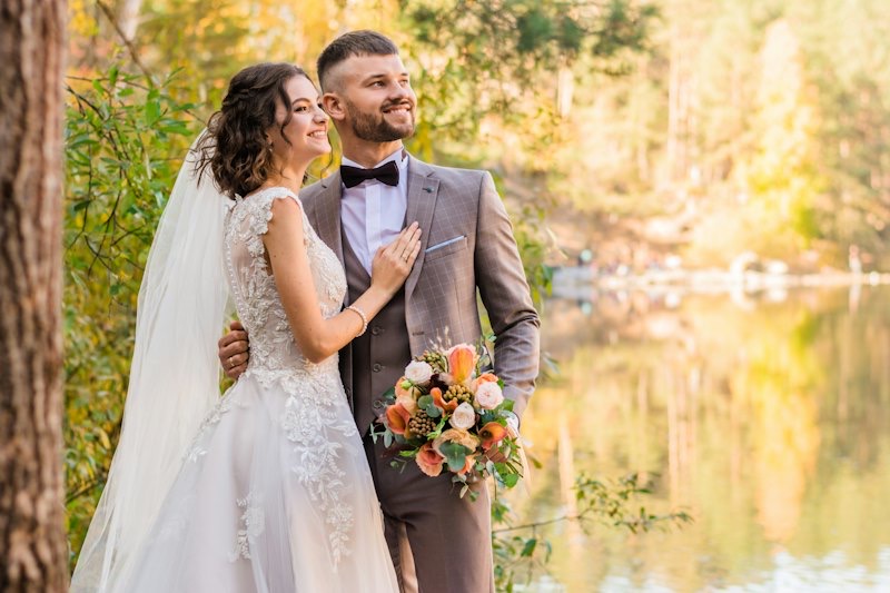 Bride and groom embracing beside a lake in autumn light