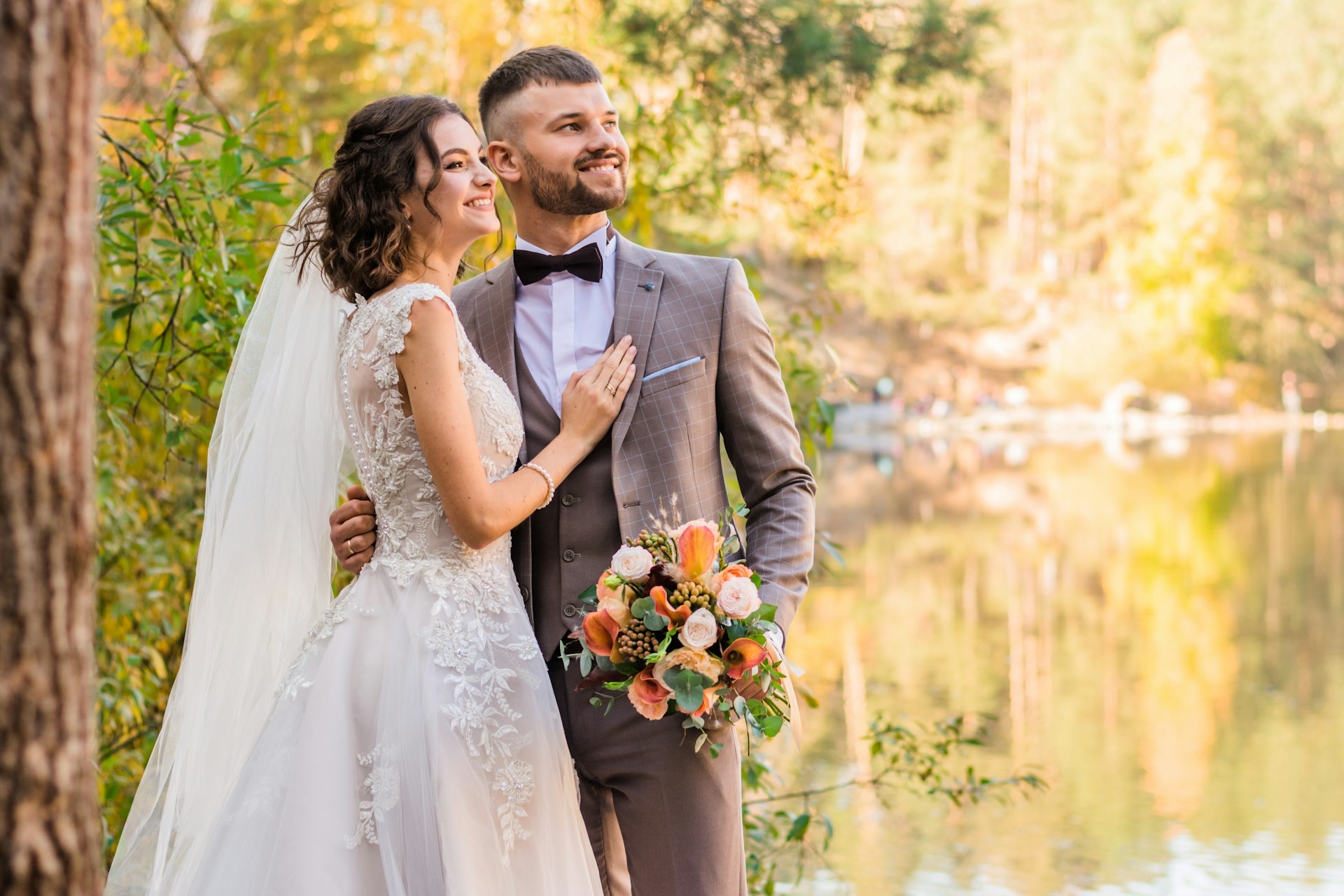 Bride and groom embracing beside a lake in autumn light