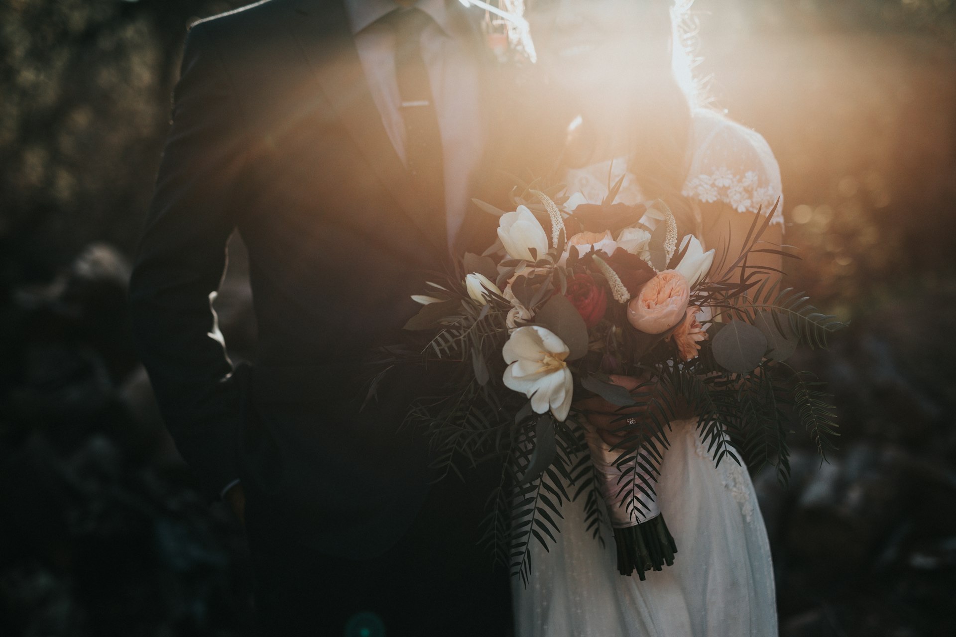 Groom beside the bride as she holds a bouquet in warm backlight