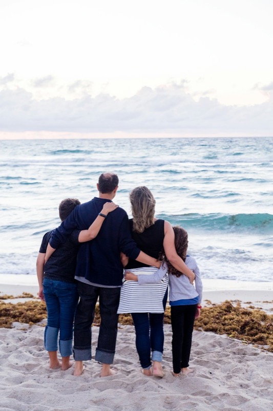A family of four hugging on the beach facing the sea