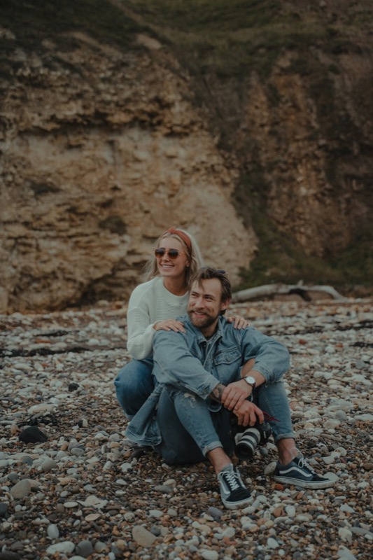 A couple sitting on rocky ground beneath a cliff