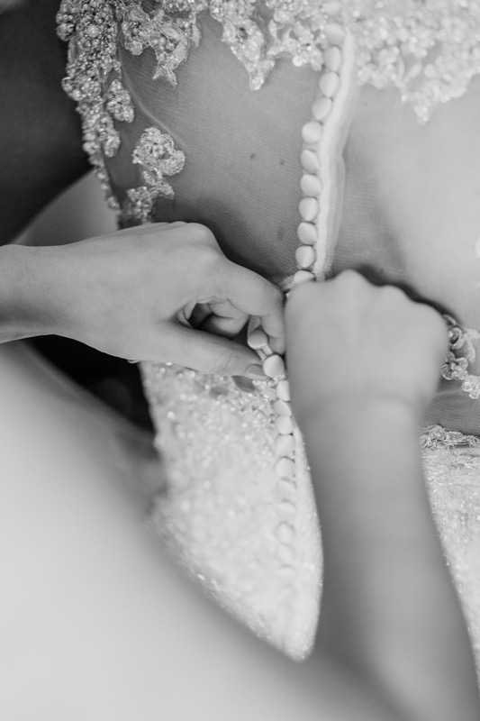Black and white close-up of hands fastening a beaded lace gown