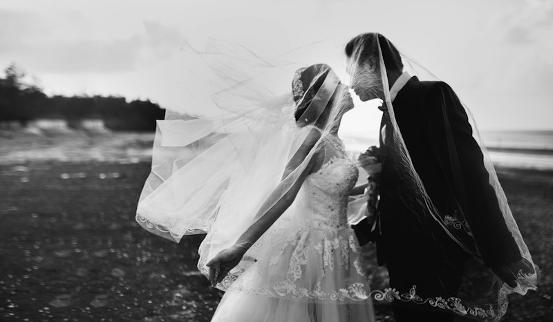 Black and white photo of a bride and groom with the veil caught in the wind