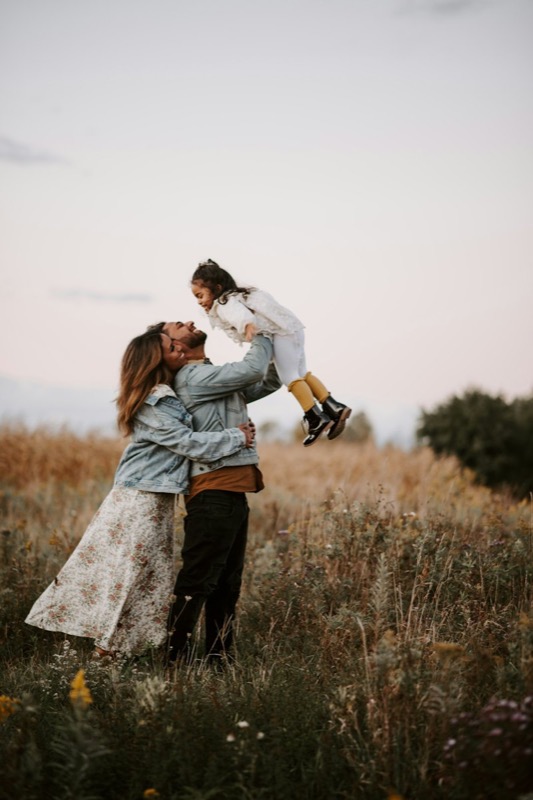 Parents lifting their child into the air in a field at dusk