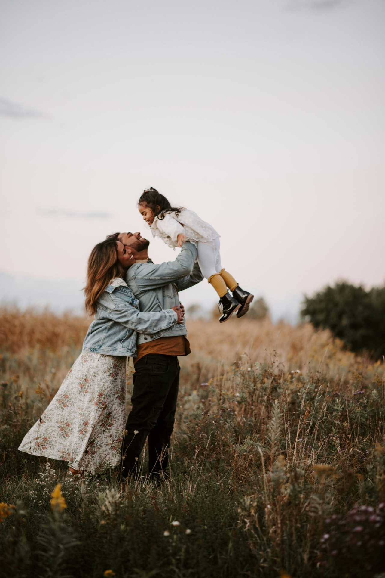 Parents lifting their child into the air in a field at dusk