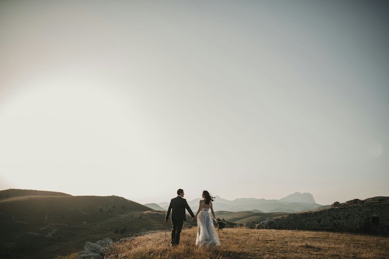 A bride and groom walking together across a hilltop under a hazy sky