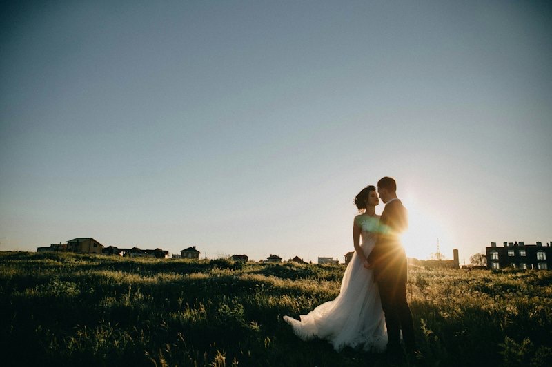 Bride and groom silhouetted by the sun on a grassy field