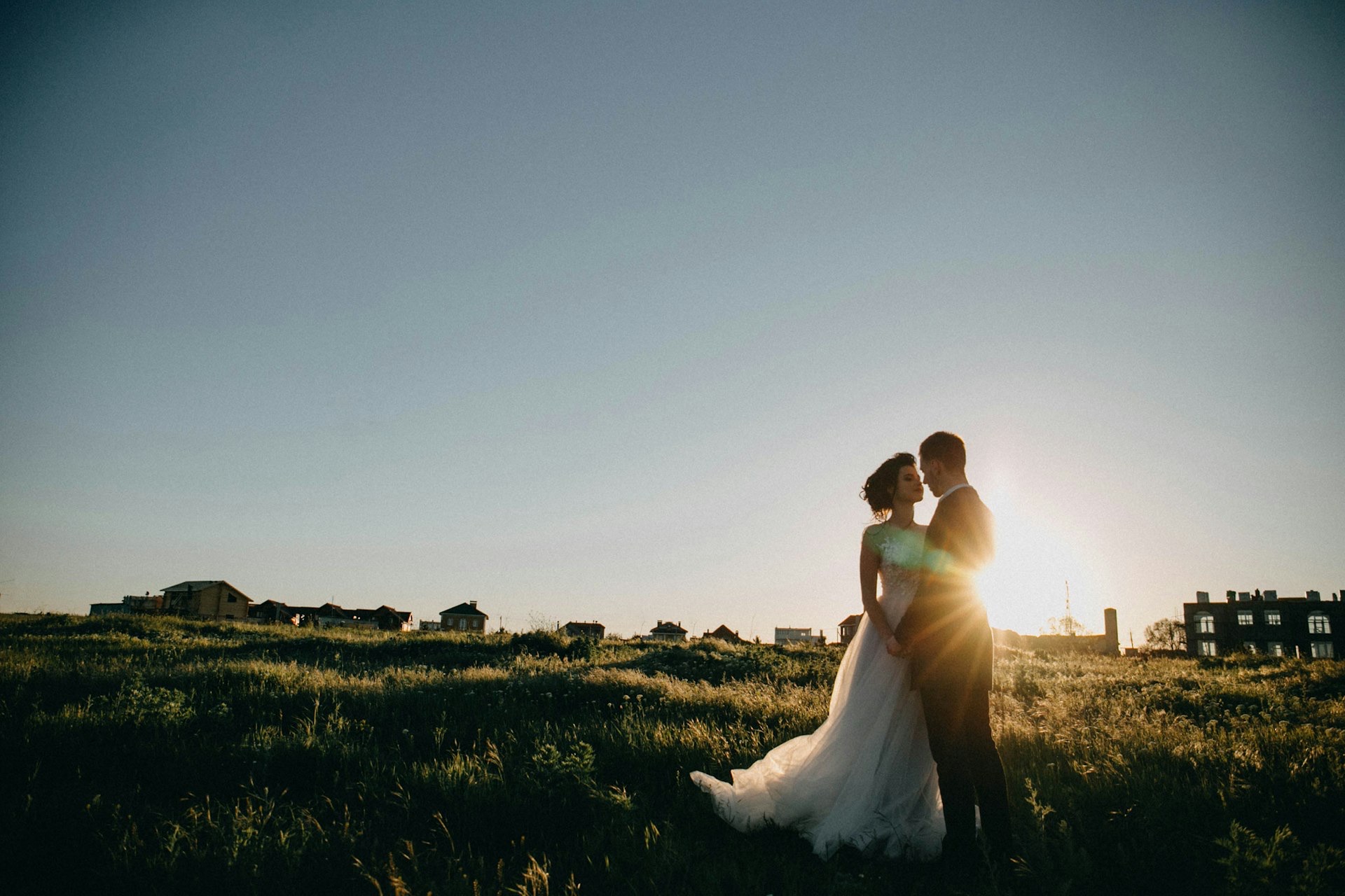 Bride and groom silhouetted by the sun on a grassy field