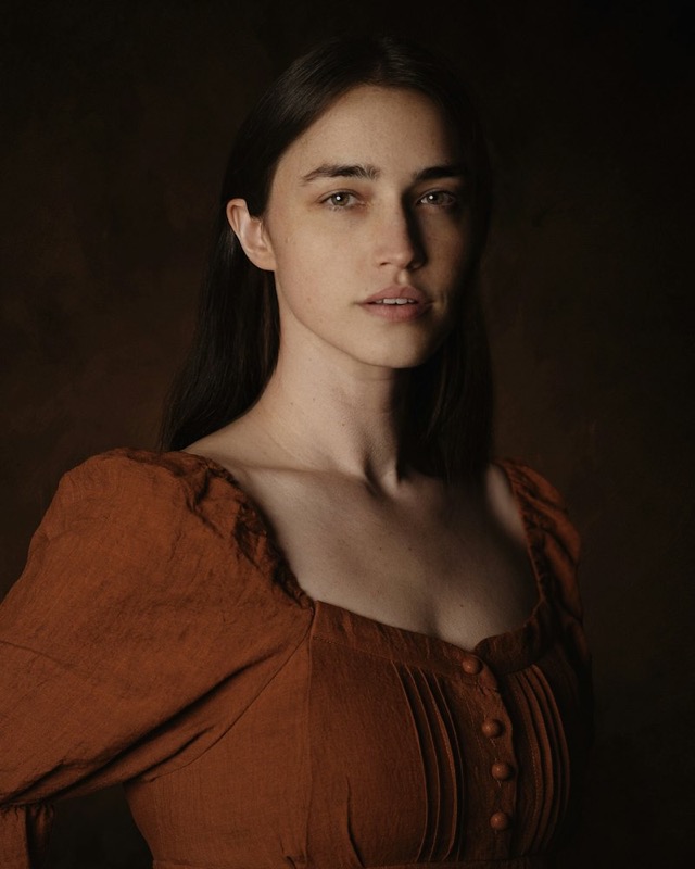Portrait of a woman in a rust-colored dress in low light