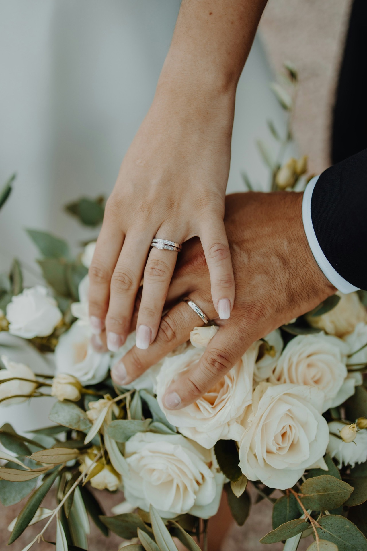 Two hands with wedding bands resting over a bouquet