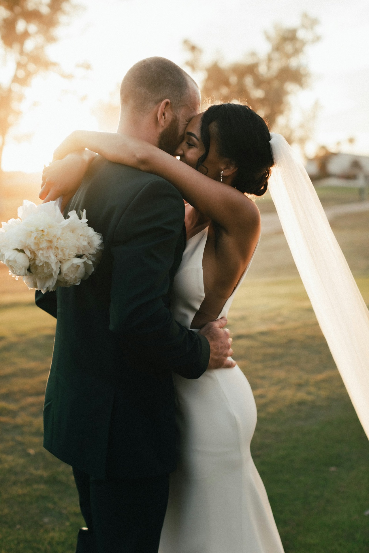 Groom holding the bride close in a sunlit meadow