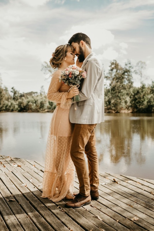 A couple standing close together on a wooden dock by the water