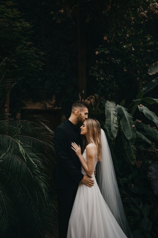 Bride and groom sharing a kiss among lush green plants